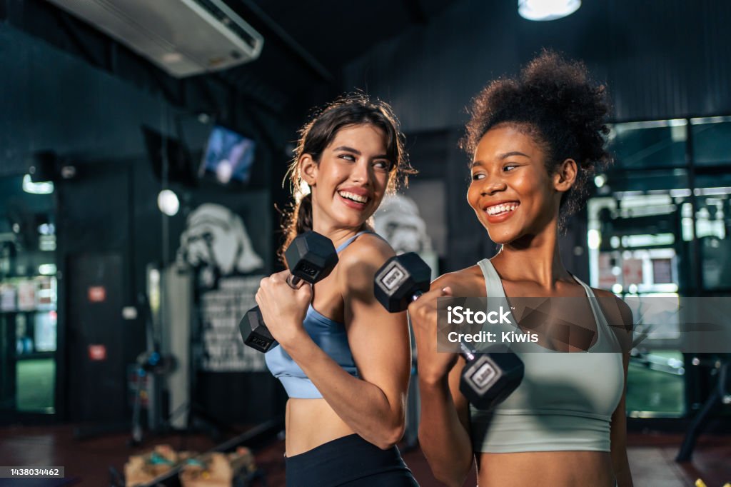 Latino and African sport woman exercising and build muscle in stadium. Active strong beautiful fit athlete girls in sportswear workout lifting weight dumbbell for arm and health care at fitness club.